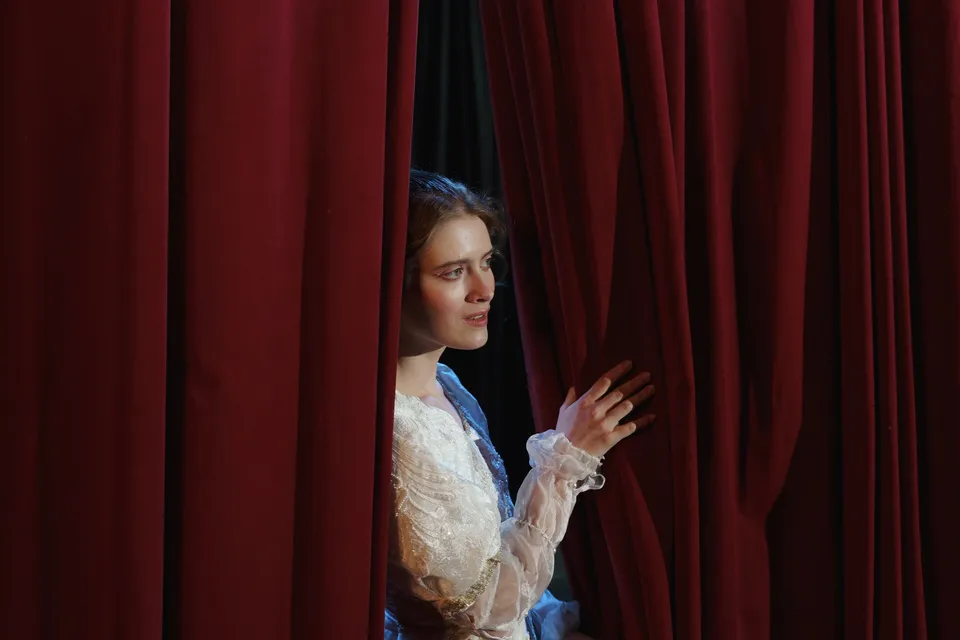 Comédienne en jeu d'une pièce de théâtre ouvrant un rideau